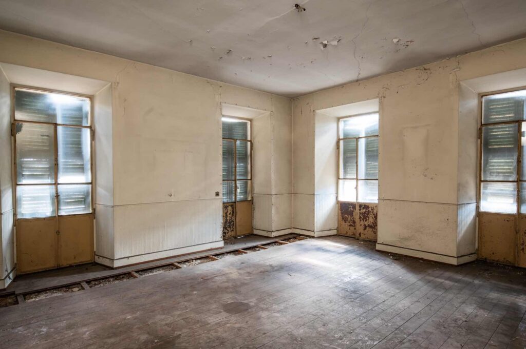 Cucina al secondo piano di Casa Varenna a Locarno prima del restauro, con pavimento in legno, finestre storiche e pareti con intonaci deteriorati.