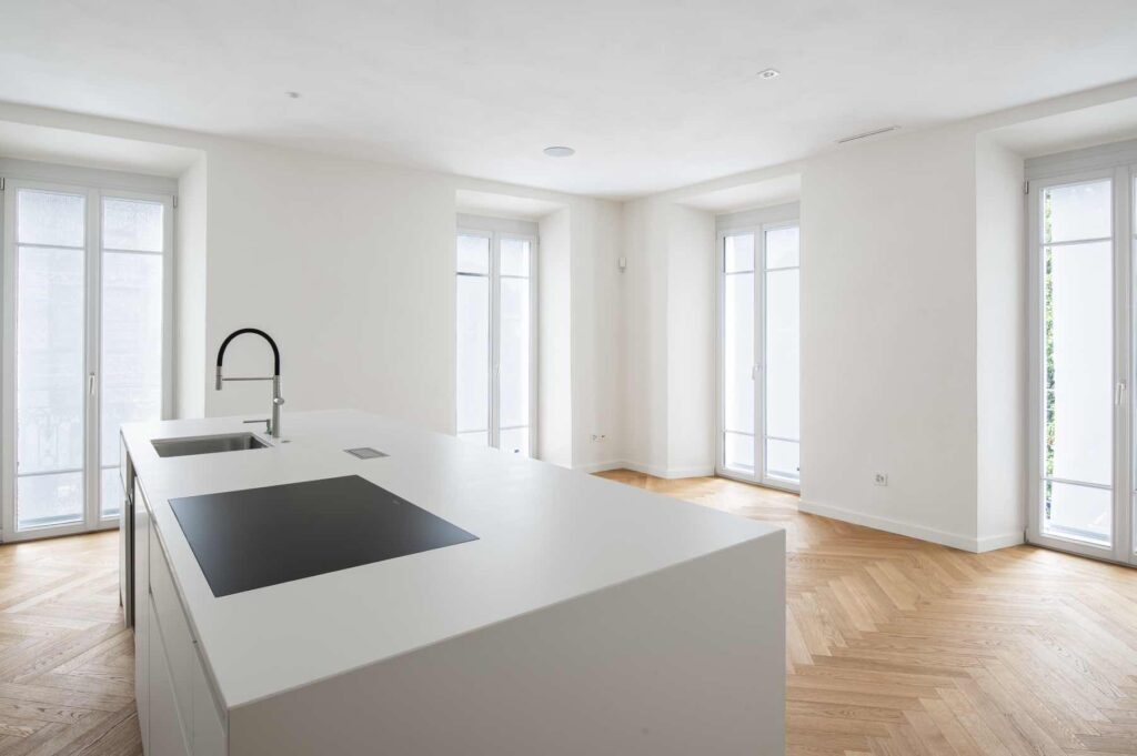 Cucina contemporanea al secondo piano di Casa Varenna a Locarno dopo il restauro, con isola centrale bianca, parquet a spina di pesce e ampie finestre.
