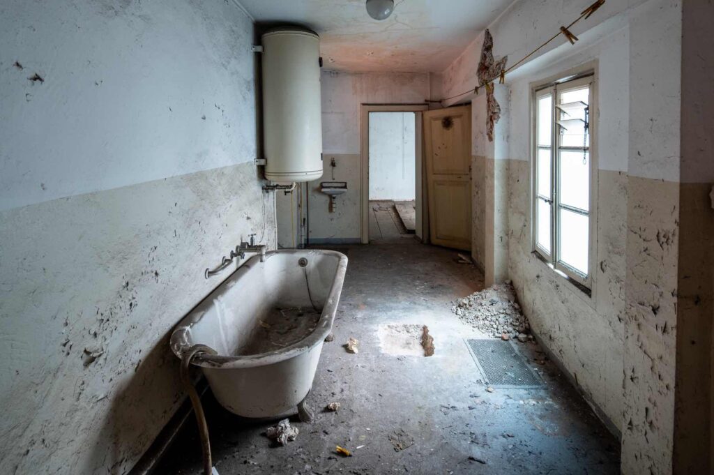 Locale al secondo piano di Casa Varenna a Locarno prima del restauro, con vecchia vasca da bagno, scaldabagno e pareti con intonaci deteriorati.