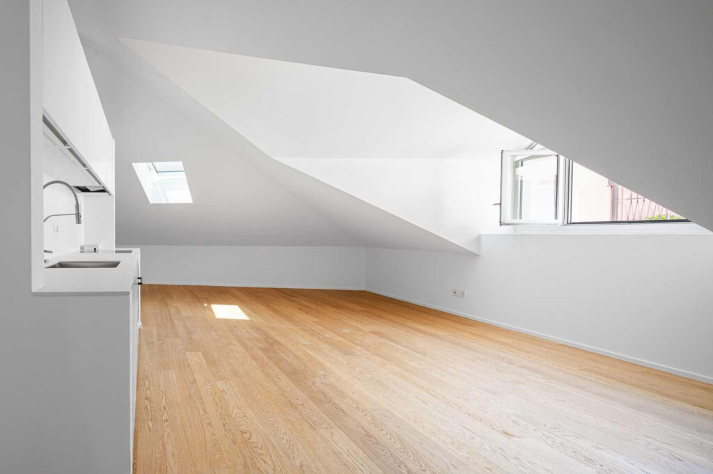 Ambiente mansardato di Casa Varenna a Locarno dopo il restauro, con soffitto inclinato, pavimento in legno e cucina integrata.