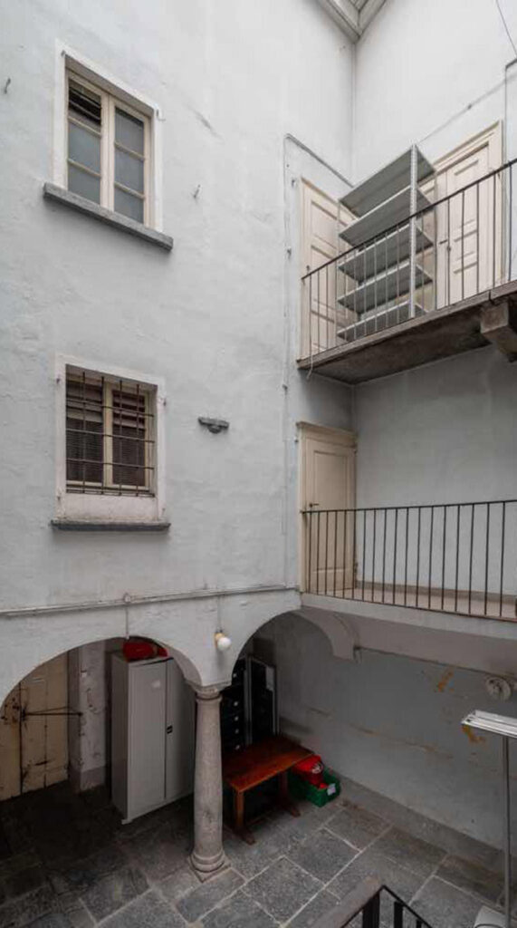 Corte interna di Casa Varenna a Locarno prima del restauro, con ballatoi sovrapposti, ringhiere in ferro, finestre storiche e porticato con colonne in pietra.