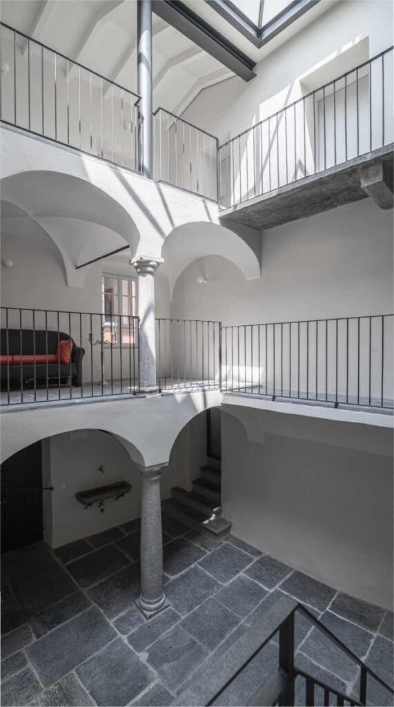 Corte interna di Casa Varenna a Locarno dopo il restauro, con colonne in pietra, porticati ad arco e ballatoio.
