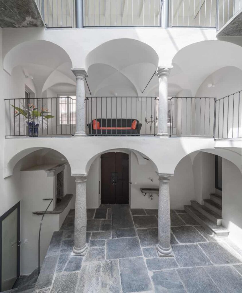Corte interna di Casa Varenna a Locarno dopo il restauro, con colonne in pietra, porticati ad arco e ballatoio.
