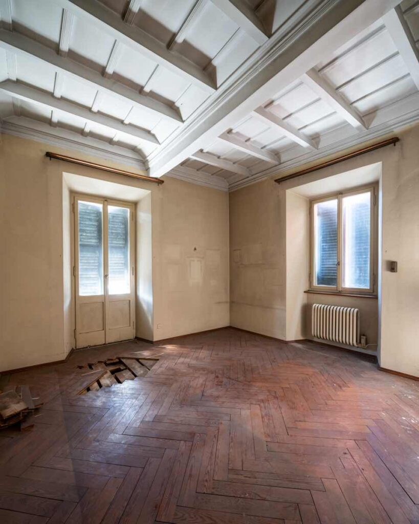 Camera al primo piano di Casa Varenna a Locarno prima del restauro, con soffitto a cassettoni in legno dipinto e pavimento in parquet.