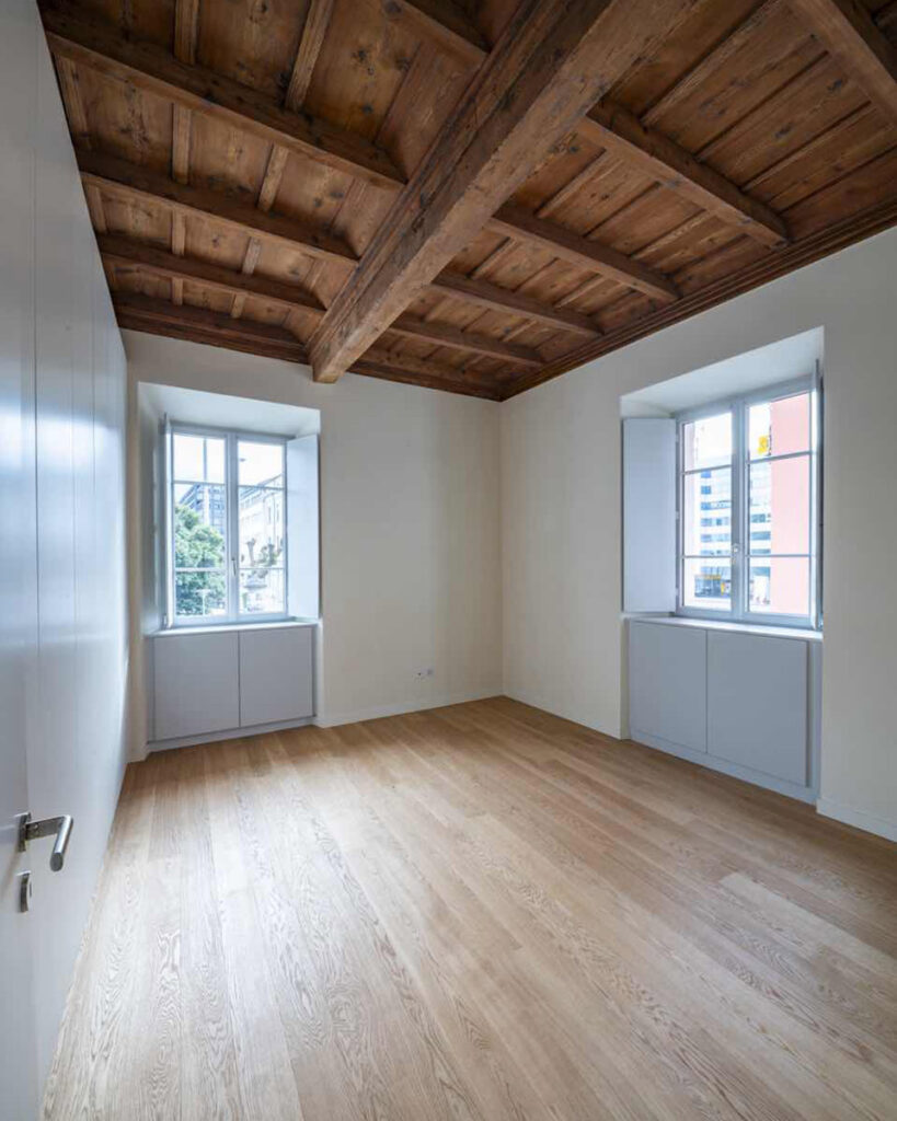 Camera al primo piano di Casa Varenna a Locarno dopo il restauro, con soffitto a cassettoni in legno e pavimento in legno.