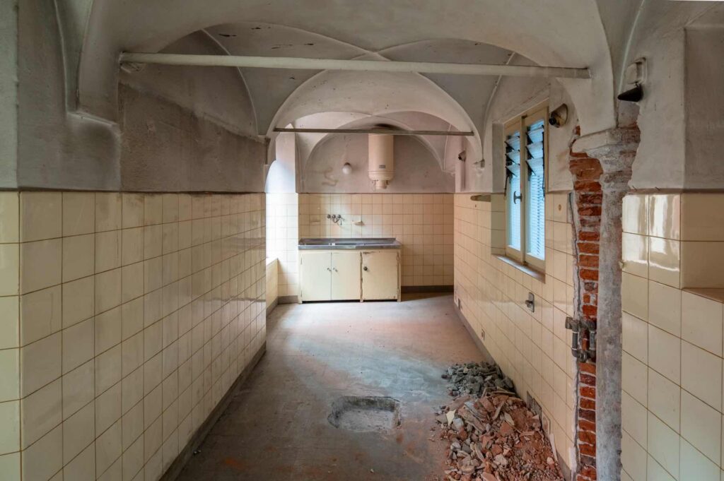 Ex cucina al primo piano di Casa Varenna a Locarno prima del restauro, con volte a crociera, pareti piastrellate e muratura a vista.