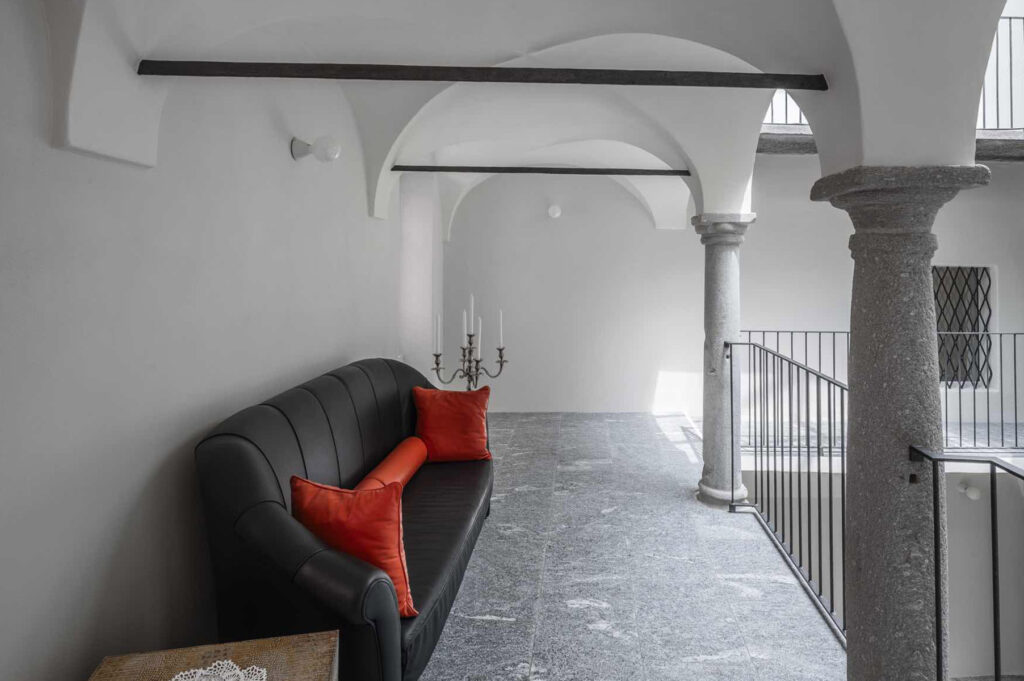 Ballatoio interno di Casa Varenna a Locarno dopo il restauro, con colonne in pietra, volte ad arco e pavimentazione in pietra.