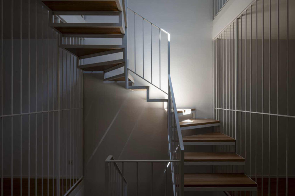 Scala interna contemporanea di Casa Varenna a Locarno dopo la ristrutturazione, con gradini in legno, struttura metallica e parapetti a elementi verticali.